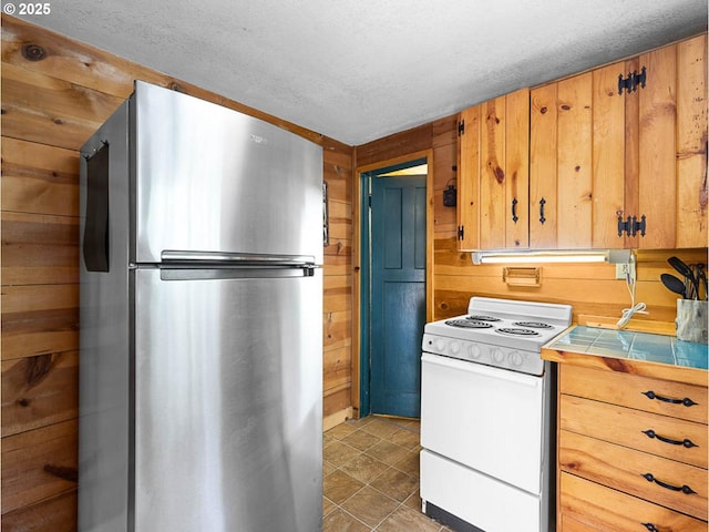 kitchen with freestanding refrigerator, electric range, wood walls, tile countertops, and a textured ceiling