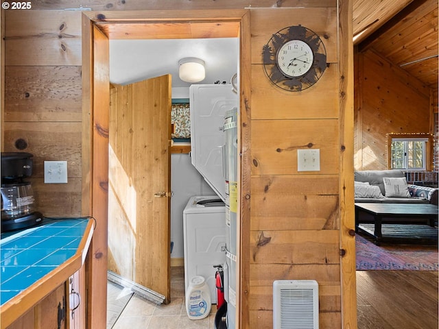 washroom with laundry area, stacked washer and dryer, light wood-style floors, and wooden walls