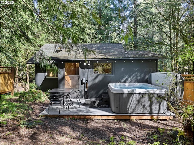 rear view of property featuring a hot tub, fence, a wooden deck, and a shingled roof