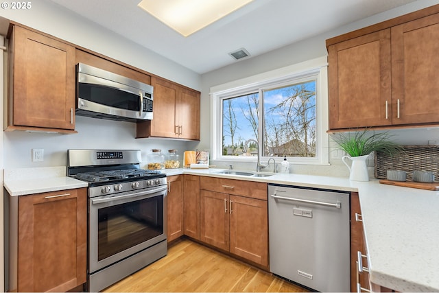 kitchen featuring brown cabinets, light wood-style flooring, a sink, appliances with stainless steel finishes, and light countertops