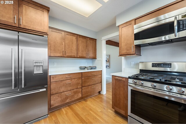 kitchen with light countertops, light wood finished floors, brown cabinets, and appliances with stainless steel finishes