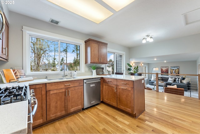 kitchen with a peninsula, a sink, stainless steel appliances, light countertops, and light wood-style floors