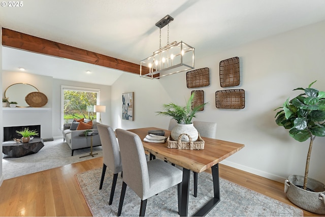 dining area featuring beam ceiling, a fireplace, baseboards, and light wood finished floors