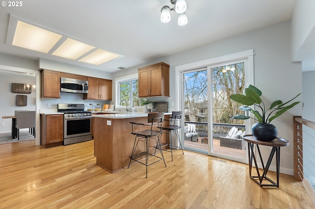 kitchen with brown cabinetry, a peninsula, appliances with stainless steel finishes, a kitchen breakfast bar, and light wood-type flooring