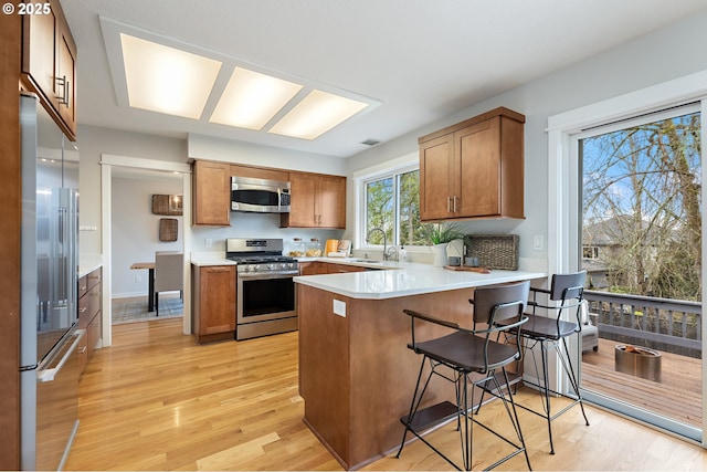 kitchen featuring a peninsula, light wood-style flooring, brown cabinetry, and appliances with stainless steel finishes