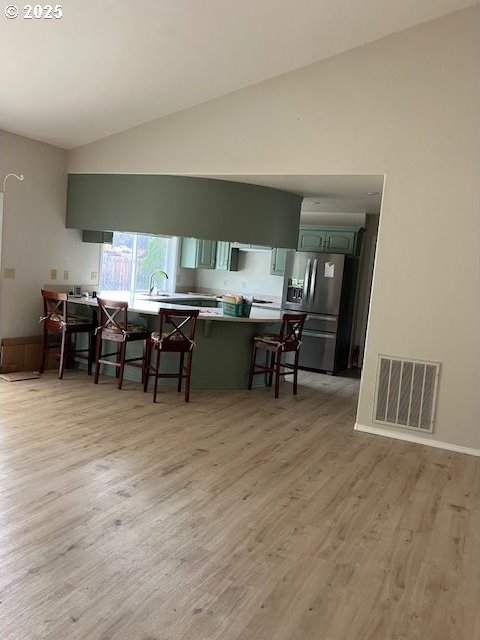 kitchen with a breakfast bar area, visible vents, lofted ceiling, stainless steel refrigerator with ice dispenser, and light wood-type flooring