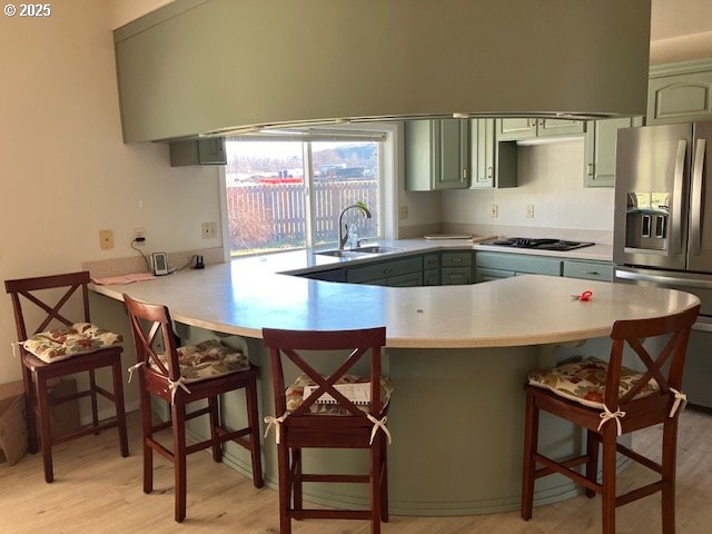 kitchen featuring a peninsula, a sink, light countertops, black gas cooktop, and stainless steel fridge