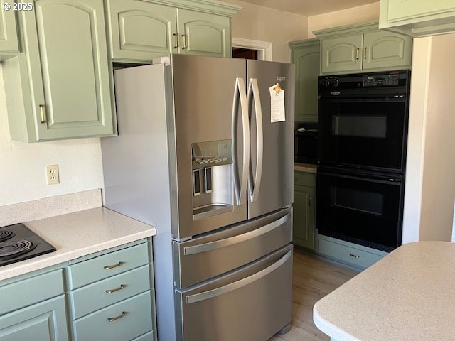 kitchen featuring green cabinets, black appliances, light countertops, and light wood-style floors