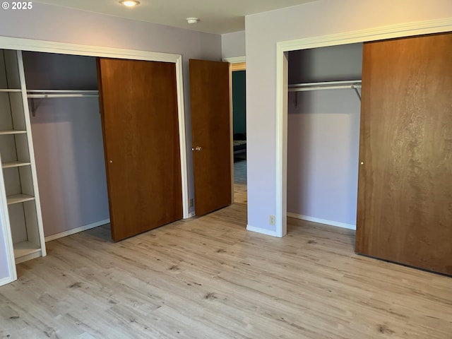 unfurnished bedroom featuring wood finished floors, baseboards, and two closets