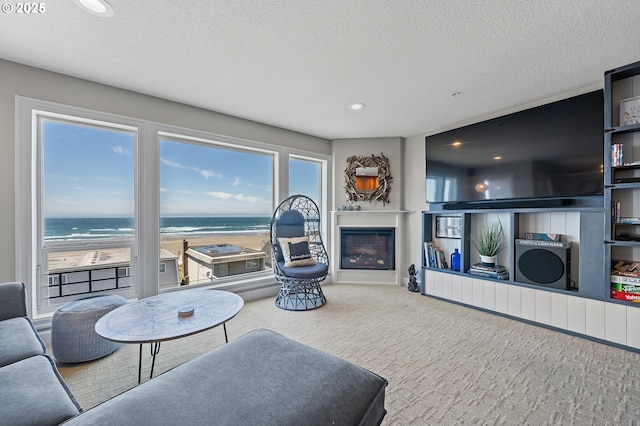 living room with a textured ceiling, a water view, a view of the beach, and carpet flooring