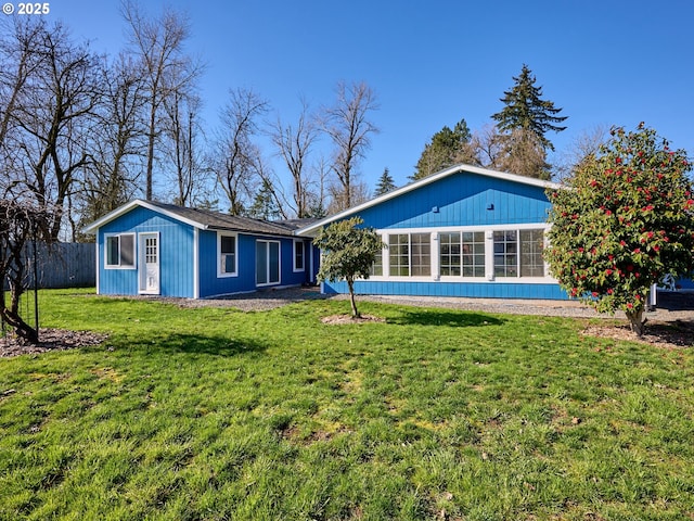 rear view of property featuring a yard, an outdoor structure, and fence