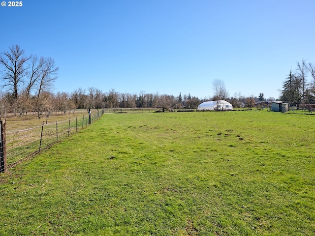 view of yard with fence, an outbuilding, and a rural view