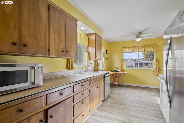 kitchen with stainless steel appliances, sink, ceiling fan, and light hardwood / wood-style flooring