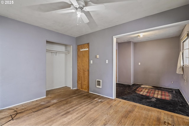 unfurnished bedroom with heating unit, hardwood / wood-style floors, ceiling fan, and a closet