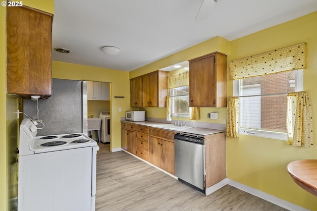 kitchen with white appliances, washer / dryer, sink, and light wood-type flooring