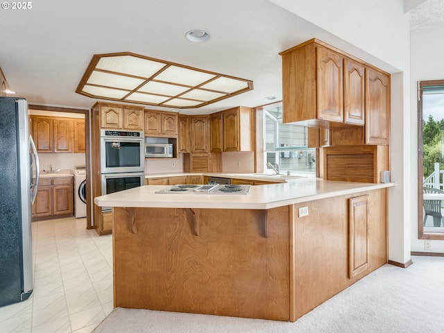 2221 NW 206th St, Ridgefield, WA 98642 - kitchen featuring appliances with stainless steel finishes, a peninsula, light countertops, a breakfast bar, and brown cabinetry