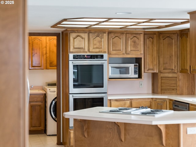 2221 NW 206th St, Ridgefield, WA 98642 - kitchen with stainless steel double oven, washer / dryer, a breakfast bar, light countertops, and white electric cooktop