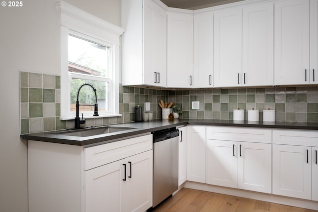 kitchen featuring tasteful backsplash, dark countertops, dishwasher, light wood-style flooring, and a sink