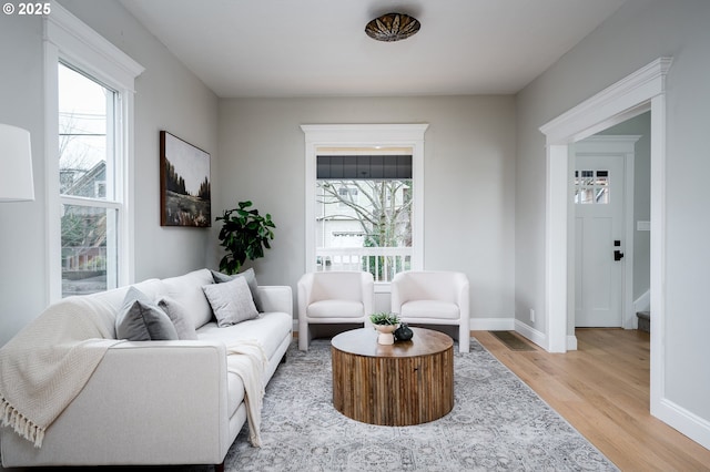 living area featuring baseboards, light wood-style floors, and a healthy amount of sunlight