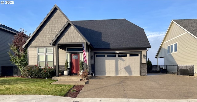 craftsman-style home featuring a garage, concrete driveway, roof with shingles, fence, and a front yard