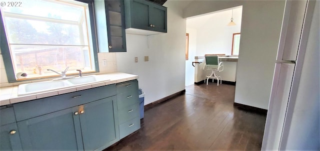 kitchen featuring tile counters, hanging light fixtures, dark wood-type flooring, and sink