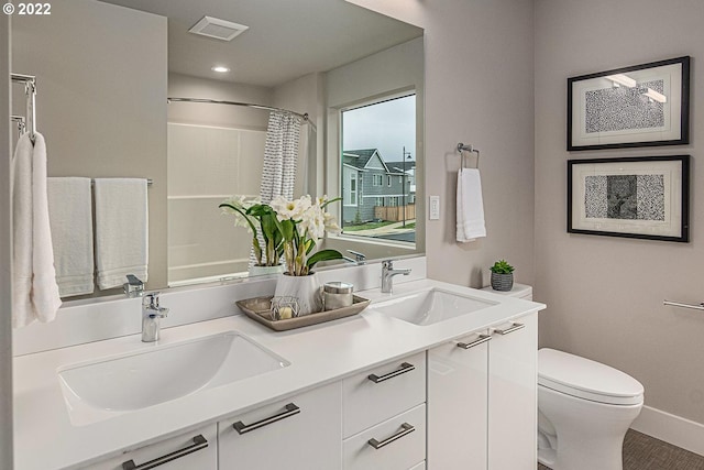 bathroom with toilet, dual sinks, and vanity with extensive cabinet space