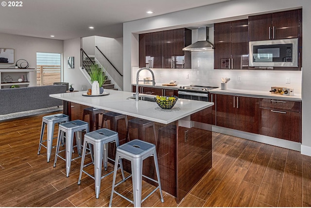 kitchen featuring a kitchen breakfast bar, stainless steel appliances, dark wood-type flooring, and wall chimney exhaust hood