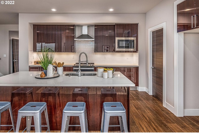 kitchen featuring a kitchen bar, stainless steel microwave, dark wood-type flooring, and wall chimney range hood