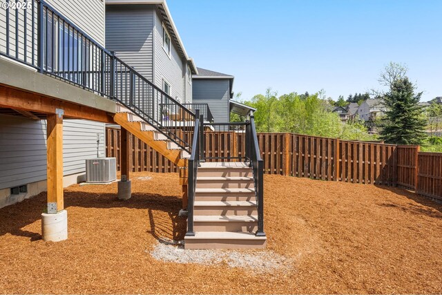 view of yard with a fenced backyard, a wooden deck, central AC, and stairway