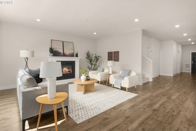 living area featuring a glass covered fireplace, recessed lighting, baseboards, wood finished floors, and stairway