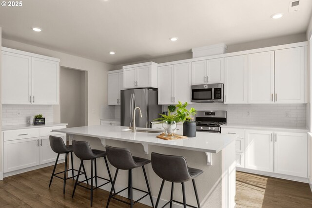 kitchen featuring backsplash, white cabinets, appliances with stainless steel finishes, and an island with sink