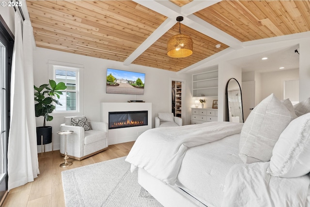 bedroom with a walk in closet, a glass covered fireplace, vaulted ceiling with beams, wood finished floors, and wood ceiling