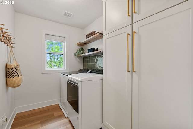 washroom with visible vents, washing machine and dryer, baseboards, light wood-type flooring, and cabinet space