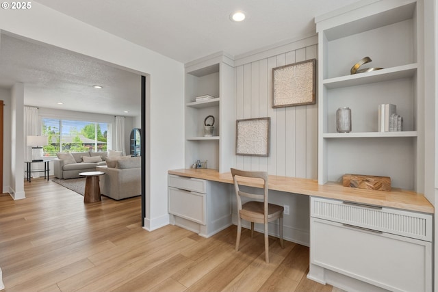 office area with baseboards, light wood-type flooring, recessed lighting, built in desk, and built in shelves