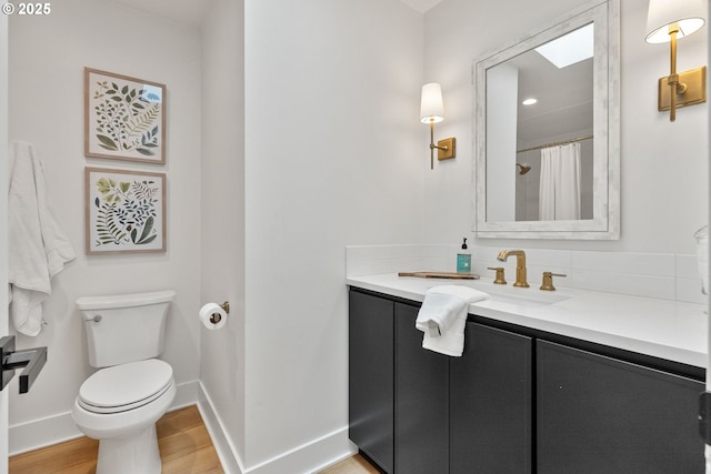 bathroom featuring baseboards, wood finished floors, toilet, and vanity