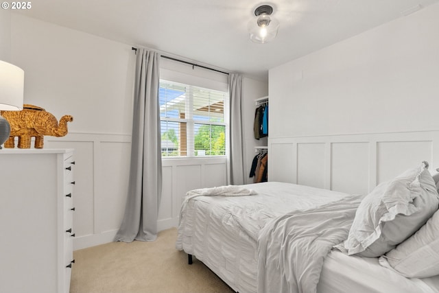 bedroom with light colored carpet, a wainscoted wall, and a decorative wall