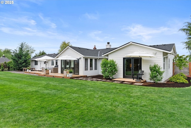 back of property with a lawn, a shingled roof, a chimney, and a deck