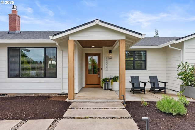 entrance to property with roof with shingles, covered porch, and a chimney