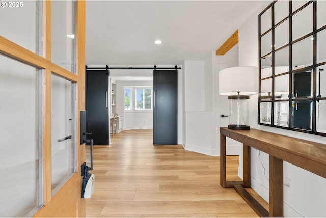 hallway featuring recessed lighting, a barn door, light wood finished floors, and baseboards