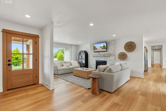 living room featuring recessed lighting, light wood finished floors, and a stone fireplace
