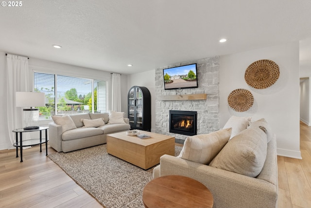 living room featuring light wood-style floors, baseboards, recessed lighting, and a stone fireplace