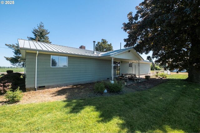 back of house featuring a standing seam roof, a chimney, a lawn, metal roof, and a patio area