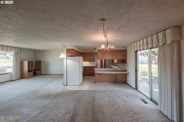 kitchen with freestanding refrigerator, plenty of natural light, a peninsula, a chandelier, and a textured ceiling