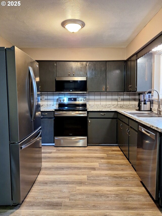 kitchen featuring tasteful backsplash, sink, stainless steel appliances, a textured ceiling, and light hardwood / wood-style flooring