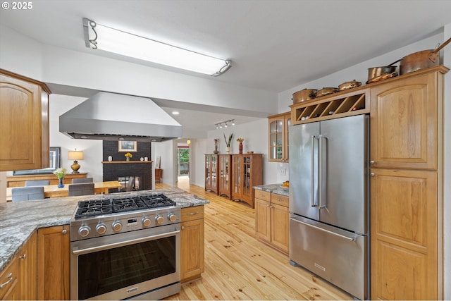 2245 SW Martha St, Portland, OR 97239 - kitchen featuring high end appliances, wall chimney exhaust hood, light wood-type flooring, light stone counters, and glass insert cabinets
