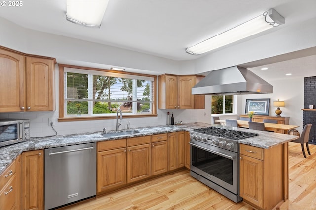 2245 SW Martha St, Portland, OR 97239 - kitchen with stainless steel appliances, wall chimney exhaust hood, light stone counters, light wood-type flooring, and a peninsula