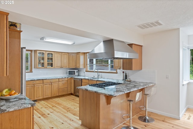 2245 SW Martha St, Portland, OR 97239 - kitchen featuring wall chimney range hood, appliances with stainless steel finishes, a peninsula, light stone countertops, and decorative backsplash