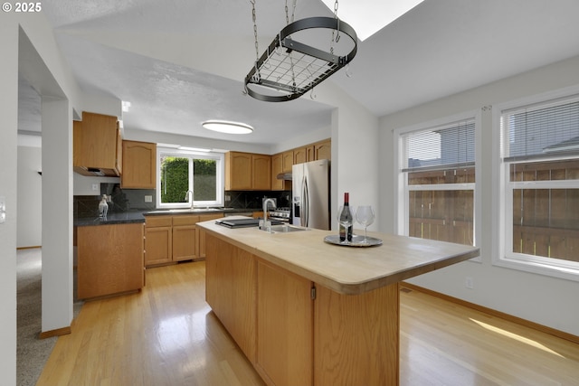 kitchen with decorative backsplash, light wood finished floors, a kitchen island with sink, and stainless steel fridge with ice dispenser