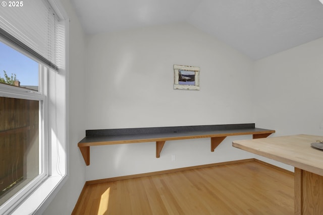 unfurnished dining area featuring baseboards, wood finished floors, and lofted ceiling