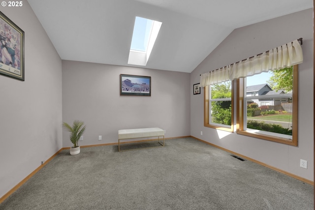 interior space featuring visible vents, baseboards, carpet floors, and vaulted ceiling with skylight